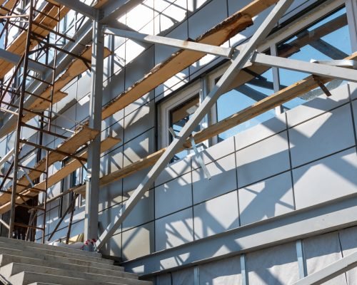 Construction of a building using scaffolding. Facade restoration work. Fragment of scaffolding and stairs against house wall. Safety at the construction site